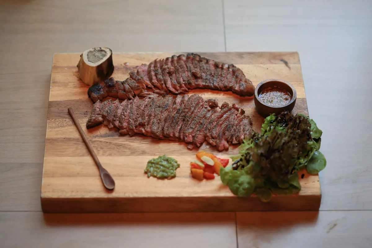 A sliced grilled steak on a wooden board with a steak knife beside it