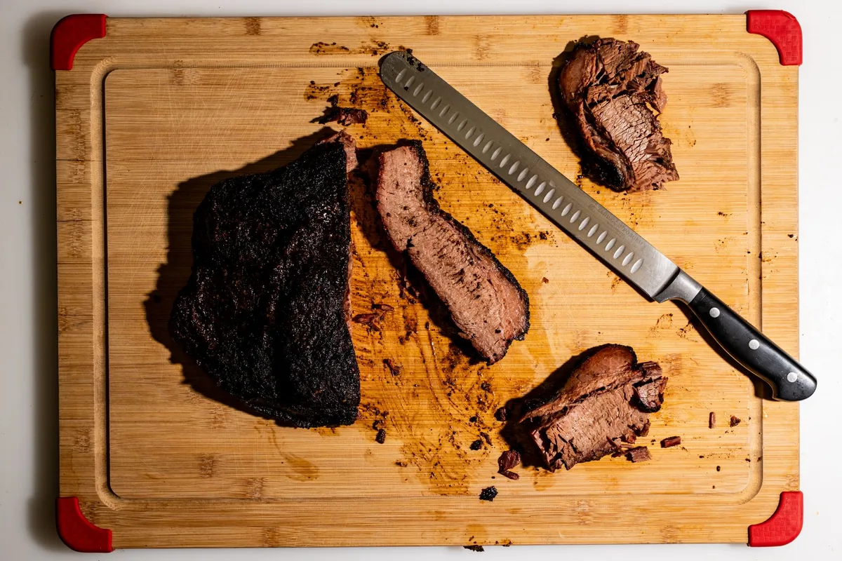 A sliced smoked brisket with a dark bark resting on a wooden board