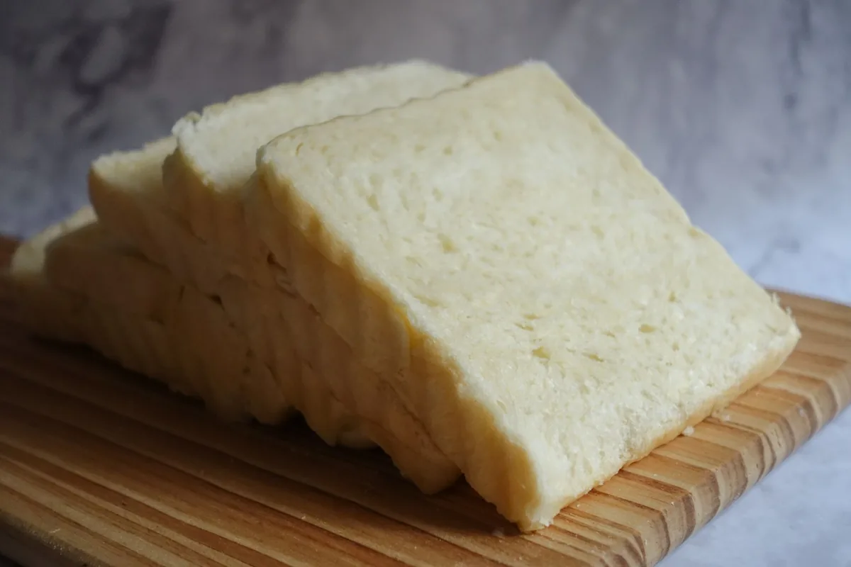 A sliced white sandwich loaf on a light surface with a few slices fanned out
