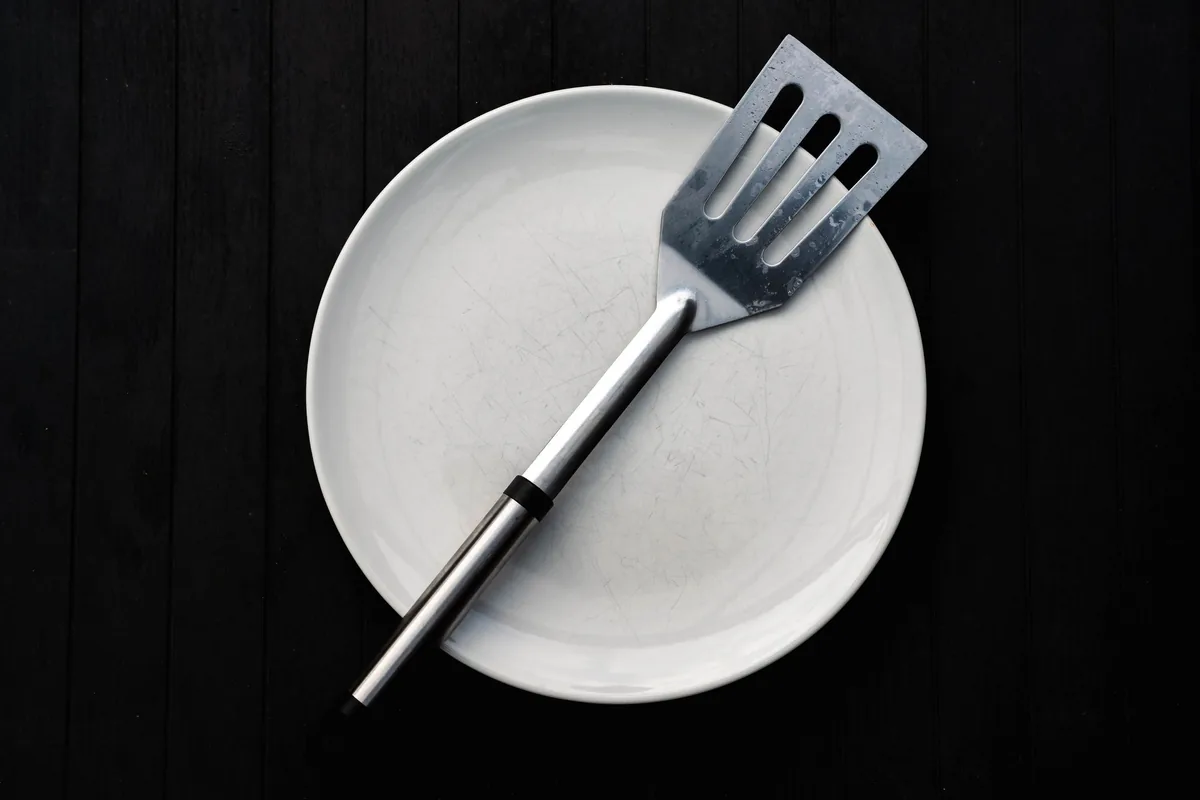 A slotted stainless steel spatula resting on a white plate