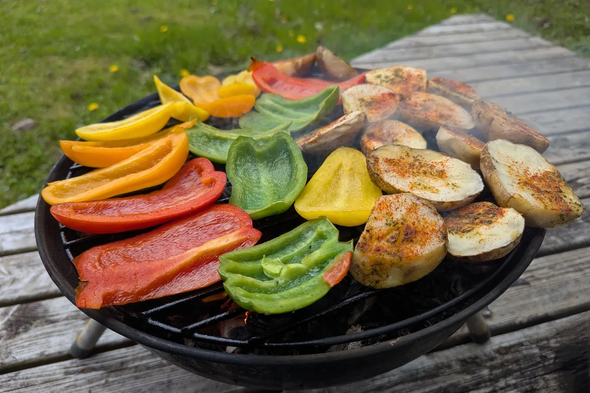 A small round charcoal grill loaded with peppers and aubergine on a wooden table