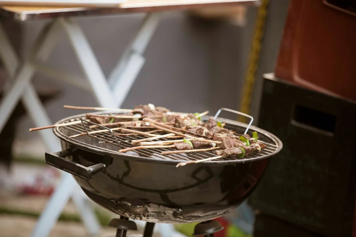 A small round grill with food on its grate on an outdoor table