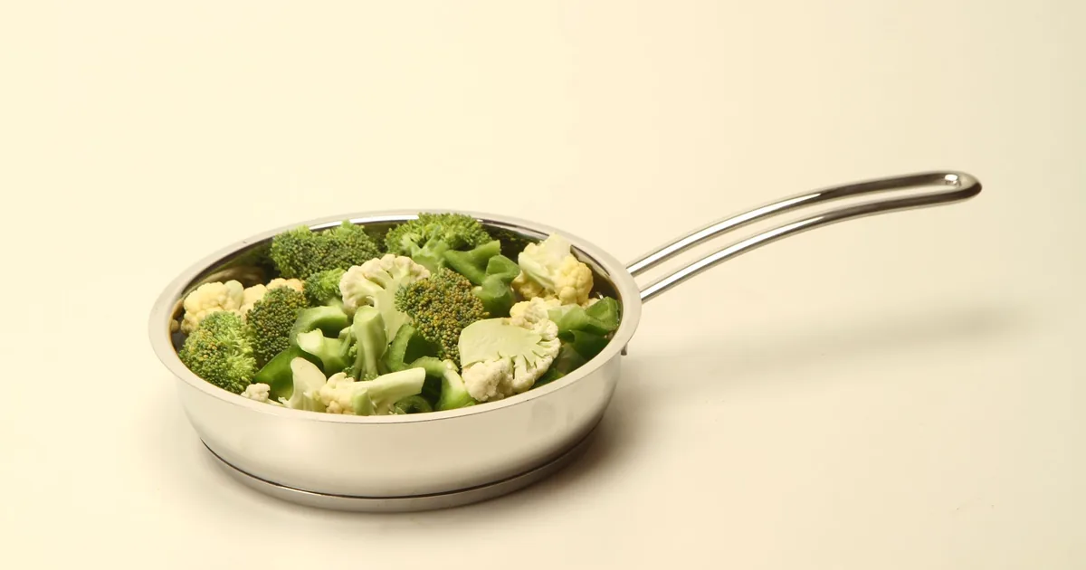 A small stainless steel pan of broccoli on a cream background