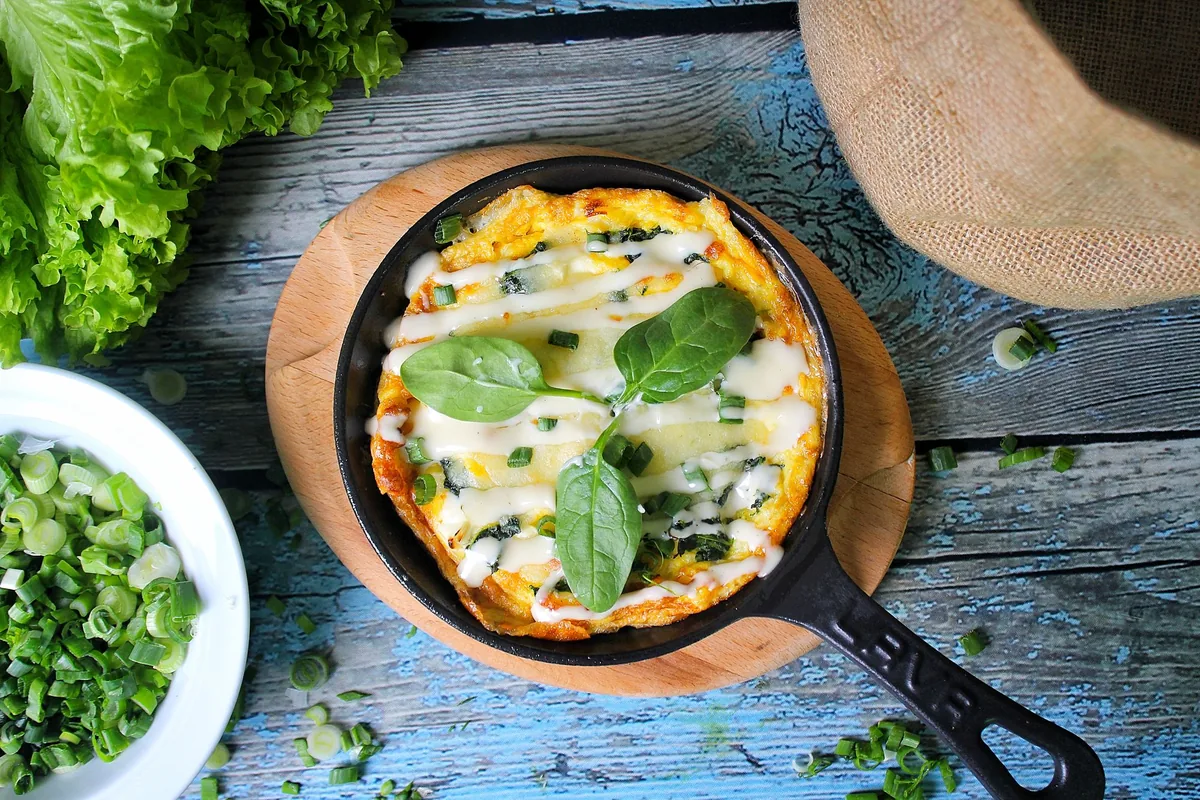 A spinach frittata in a cast iron pan on a blue table