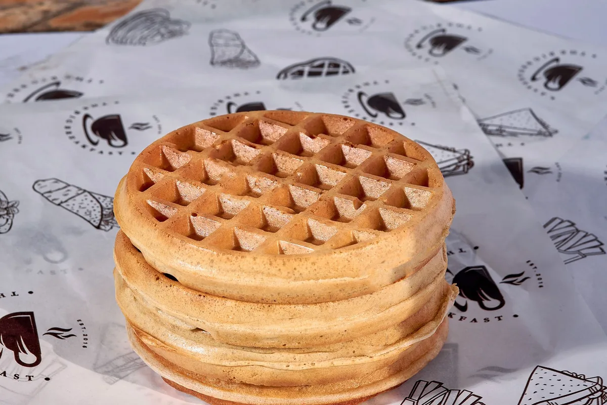 A stack of crisp waffles with syrup on a light wooden board in daylight