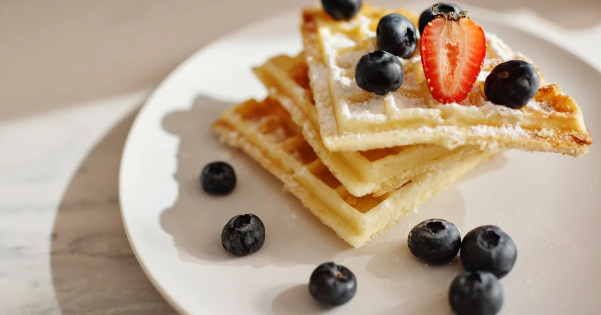 A stack of golden waffles on a white plate on a bright breakfast table