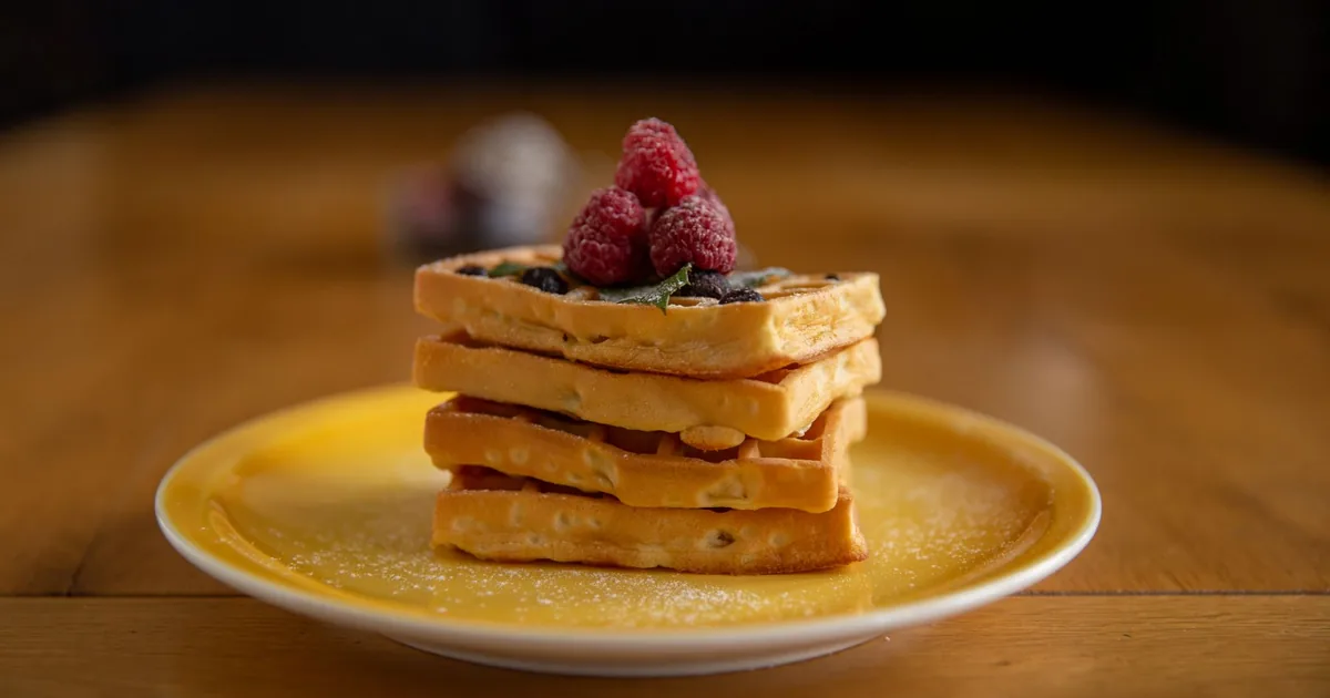A stack of square golden waffles topped with fresh berries on a white plate on a breakfast table