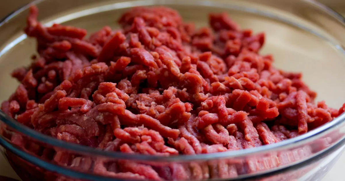 A stainless steel bowl filled with freshly ground red beef on a kitchen worktop