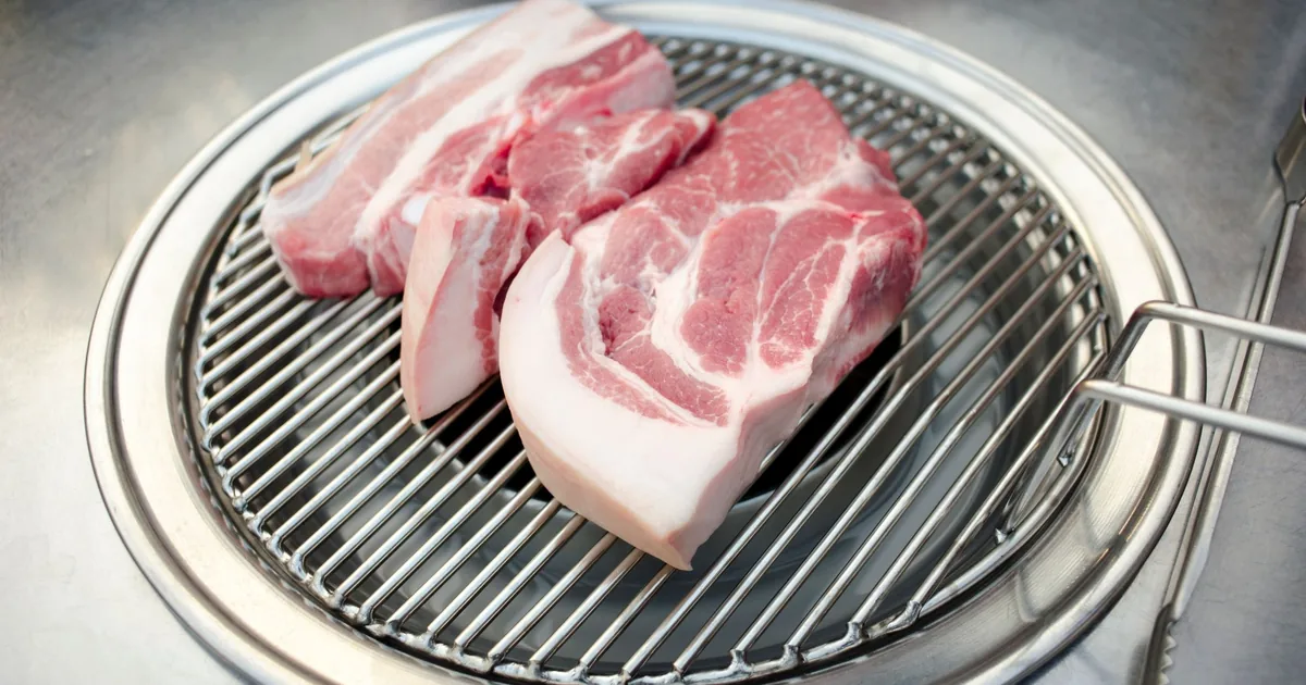 Raw pork chops on a round stainless grill grate