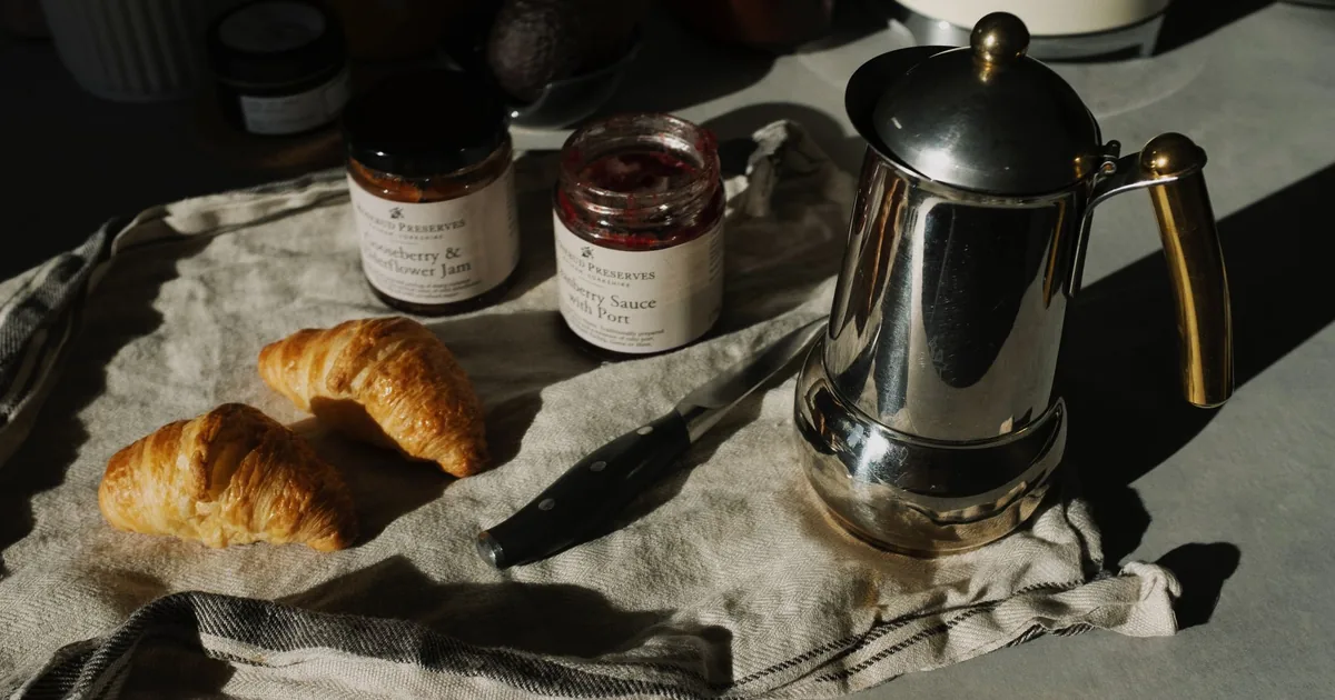 A stainless steel coffee pot beside croissants on a breakfast table