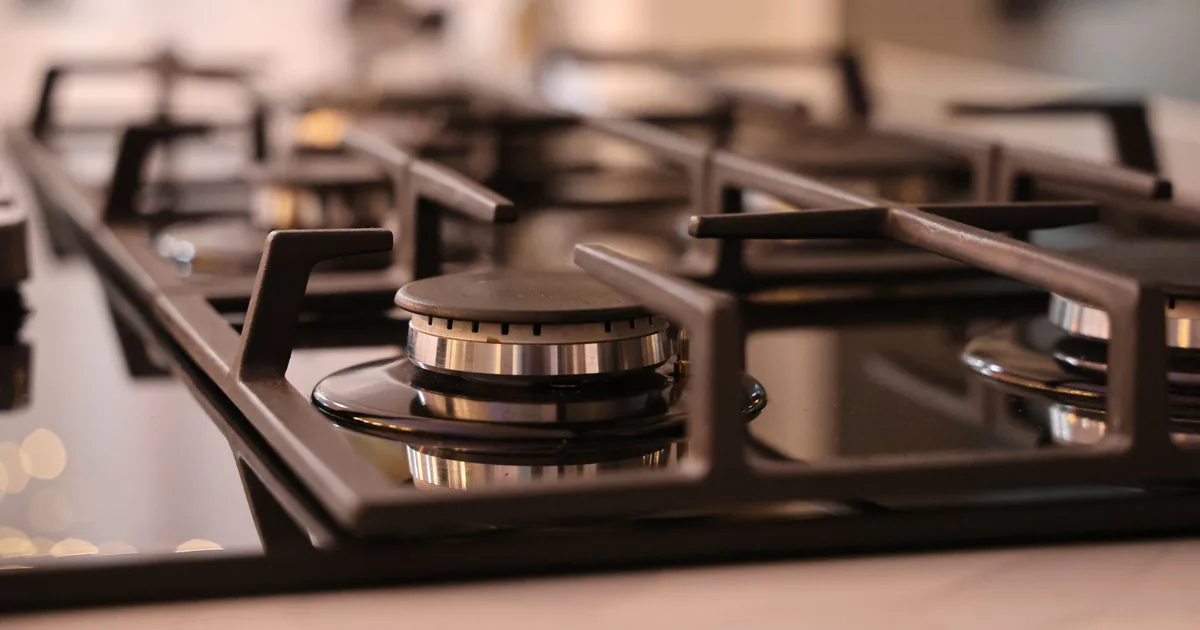 A gas cooktop with black grates and a polished burner cap