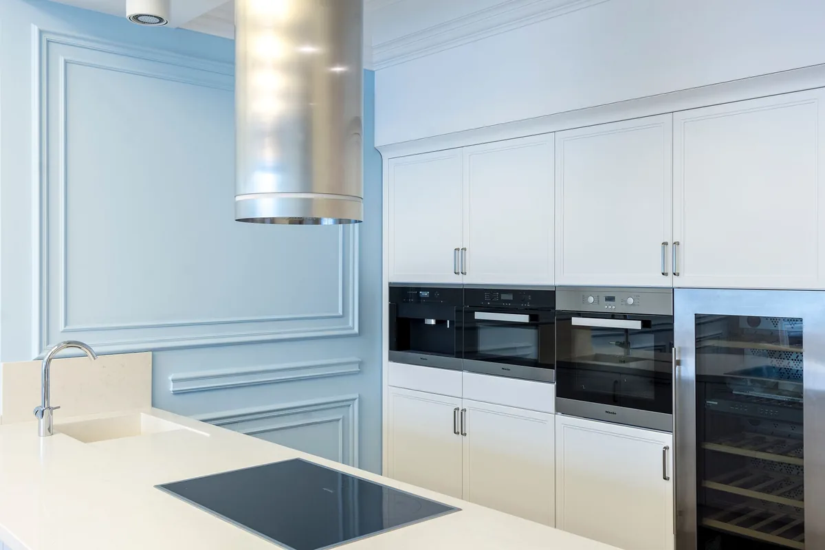 A white kitchen with a chimney hood and built-in ovens