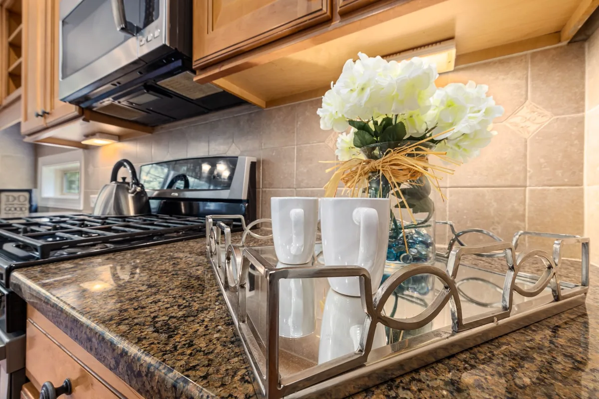 A granite counter with a tray of white mugs and flowers