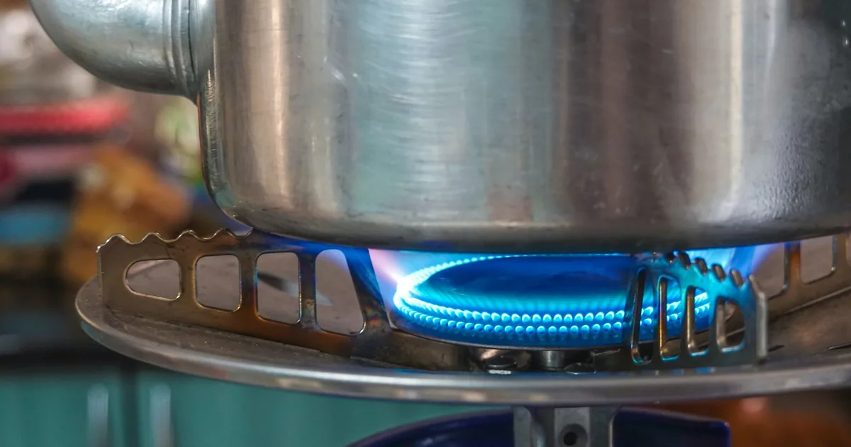 A stainless steel pot sitting on a gas hob with a ring of blue flame beneath it
