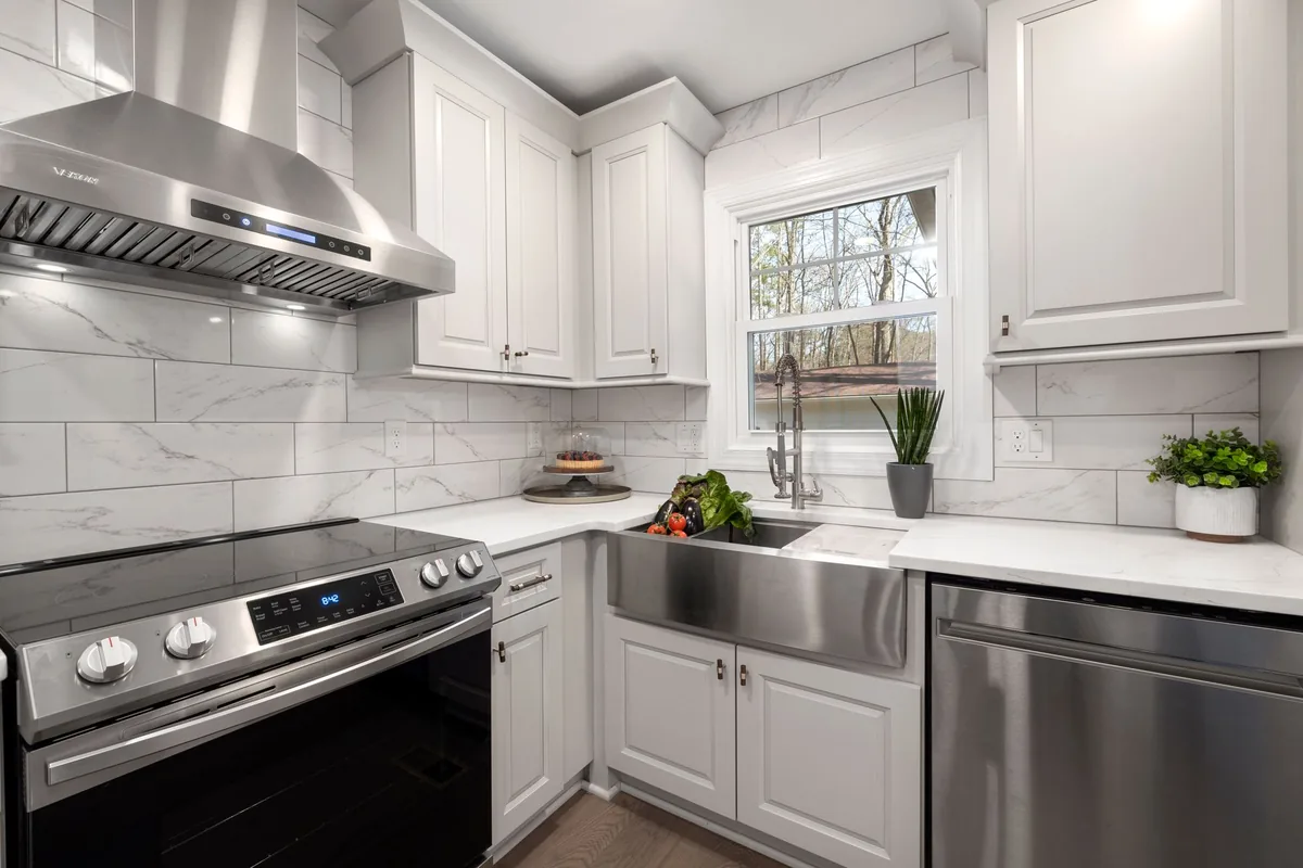A stainless steel range hood mounted above a gas cooktop against a tiled wall