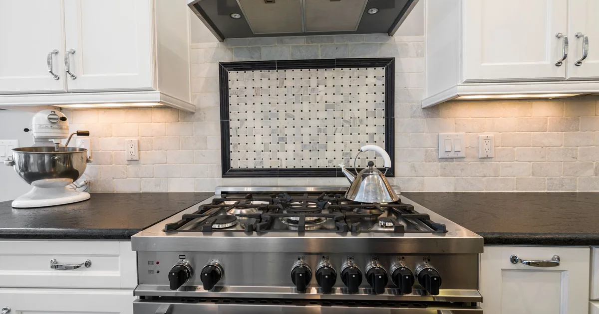A stainless gas range below a hood with a tiled backsplash