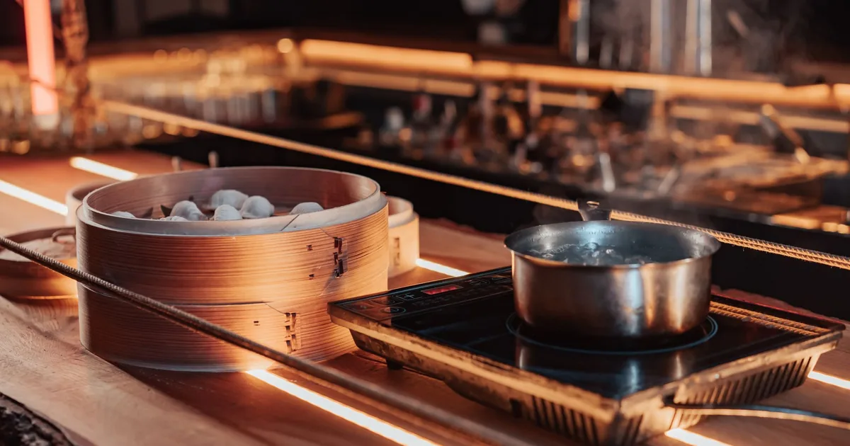 A steel pot on an induction burner beside a bamboo steamer