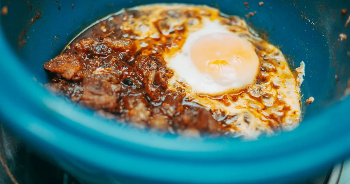 A stew topped with an egg in a teal ceramic pot