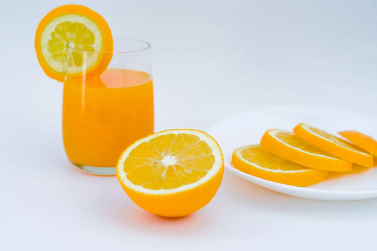 A tall glass of fresh orange juice beside sliced oranges on a light table