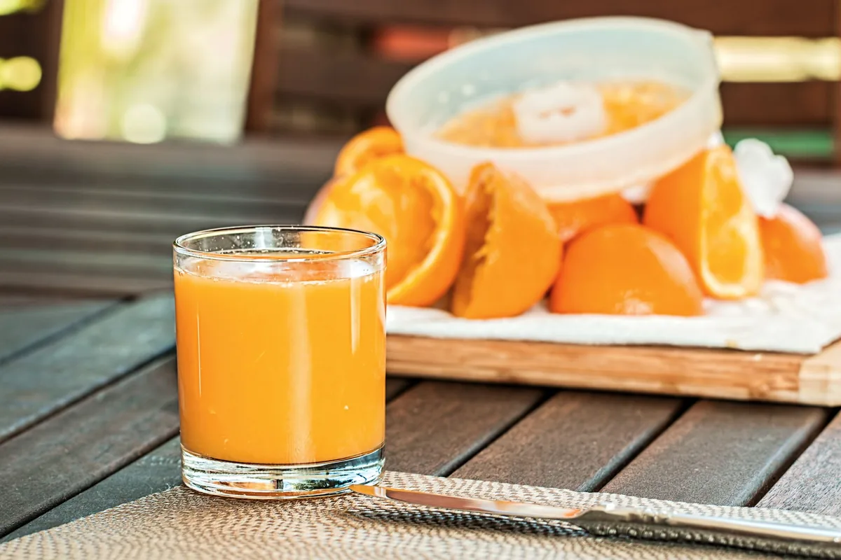 A tall glass of fresh orange juice next to halved oranges on a counter