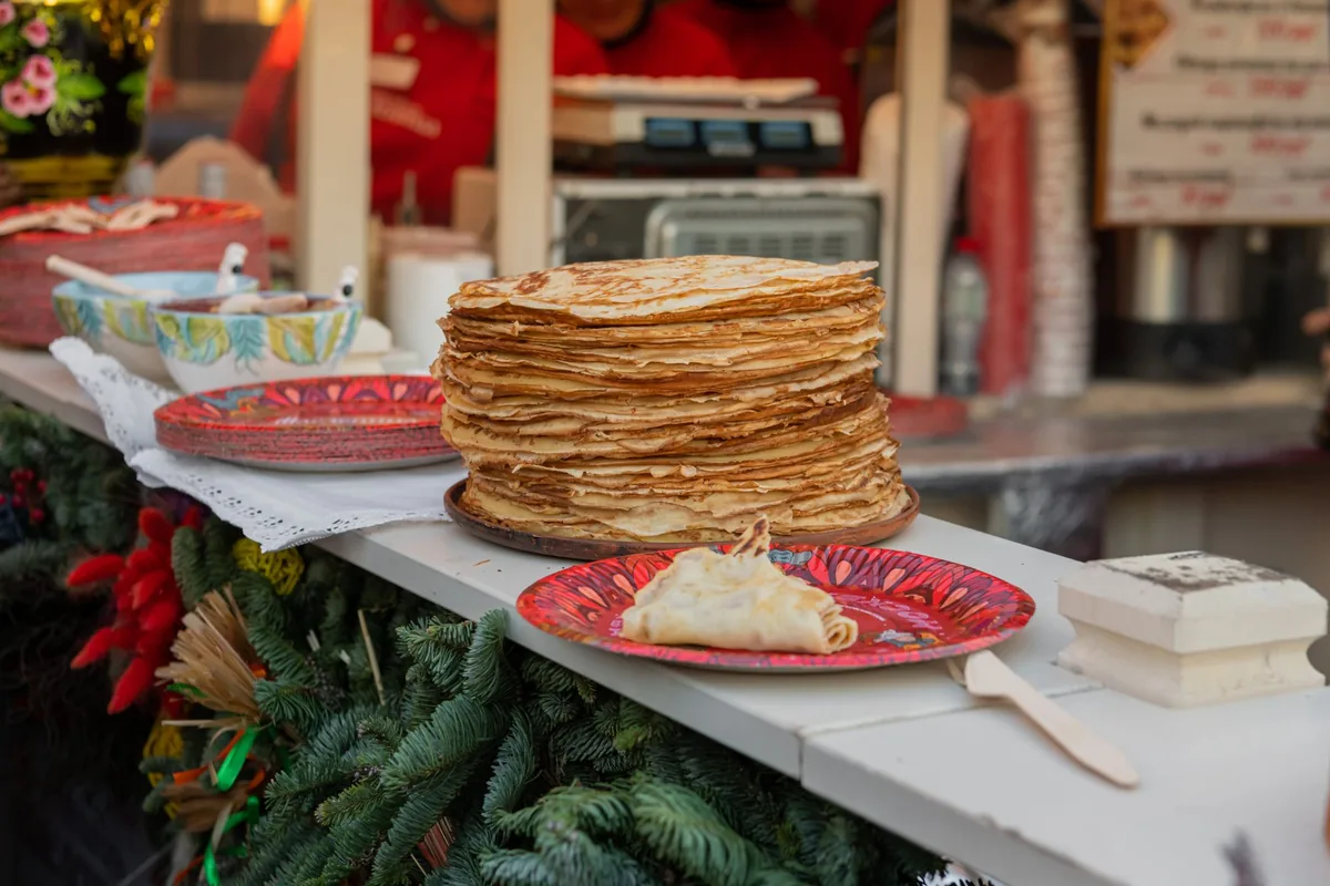 A tall stack of thin folded crepes on a plate on a bright breakfast table
