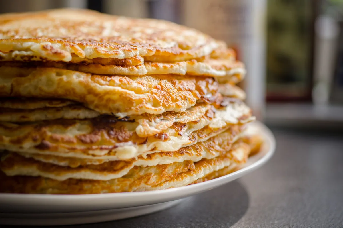 A tall stack of thin golden pancakes on a white plate
