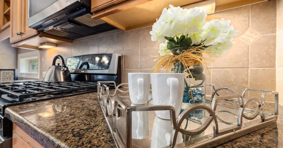 A granite kitchen counter with white mugs on a tray and flowers