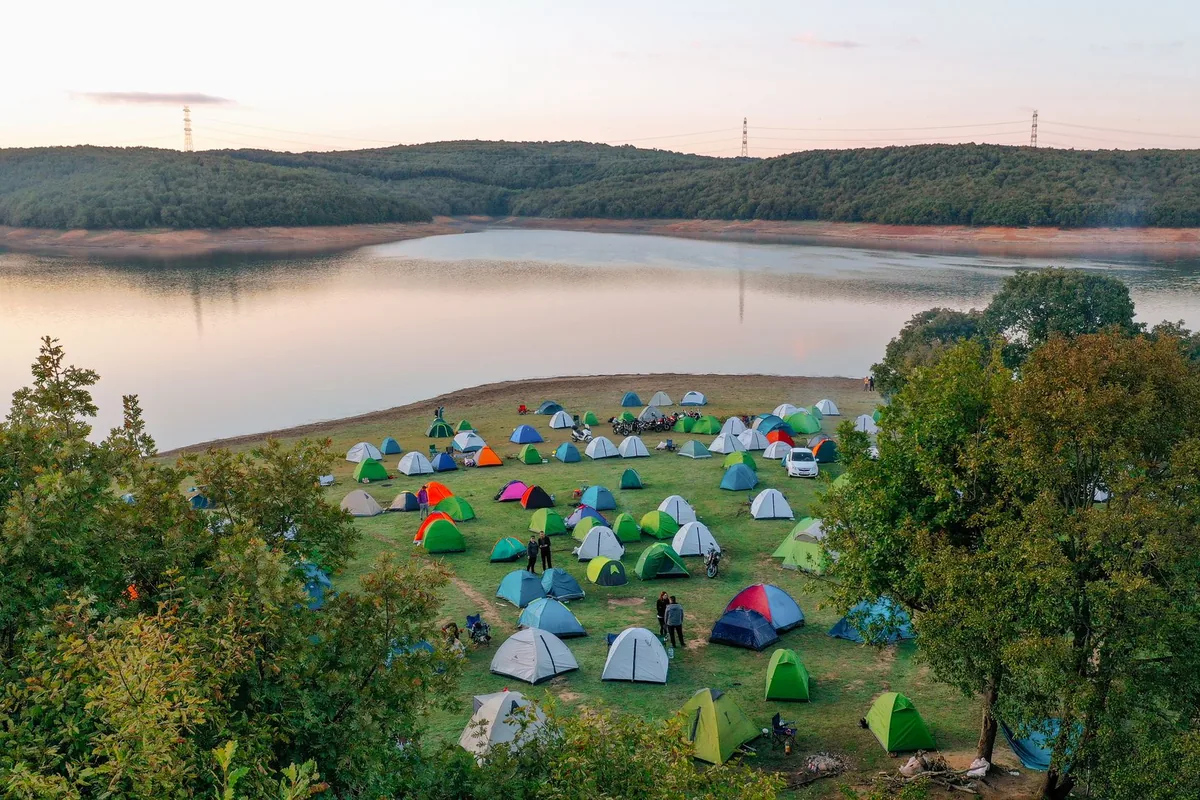 A tent pitched beside a lake on a bright day with an open grassy area in front