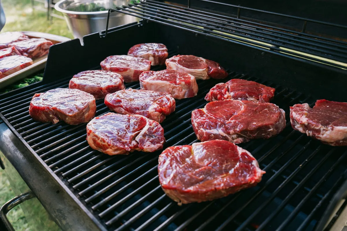 Raw steaks laid out on a large gas grill grate