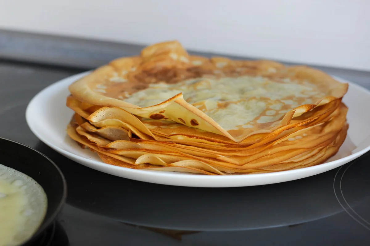 A thin golden crepe cooking in a round flat pan on a stovetop