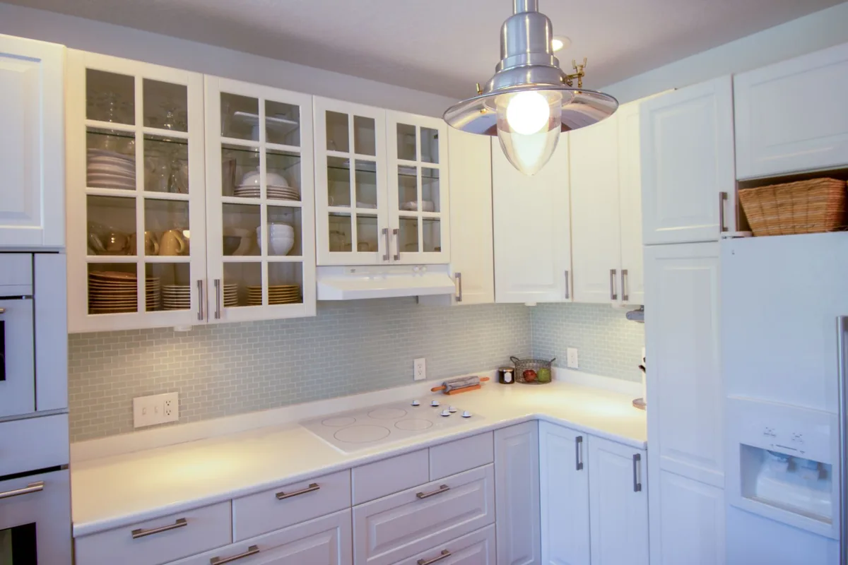 A white kitchen with glass-front cabinets and a pendant light