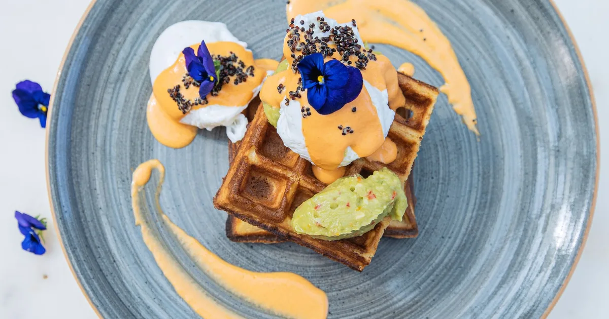 A waffle topped with fruit and edible flowers on a blue plate