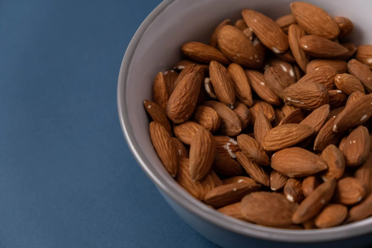 A white bowl filled with raw whole almonds on a light kitchen counter