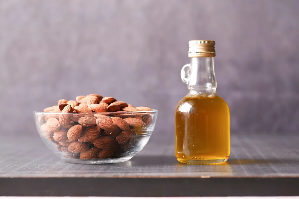 A white bowl filled with raw whole almonds on a light wooden table