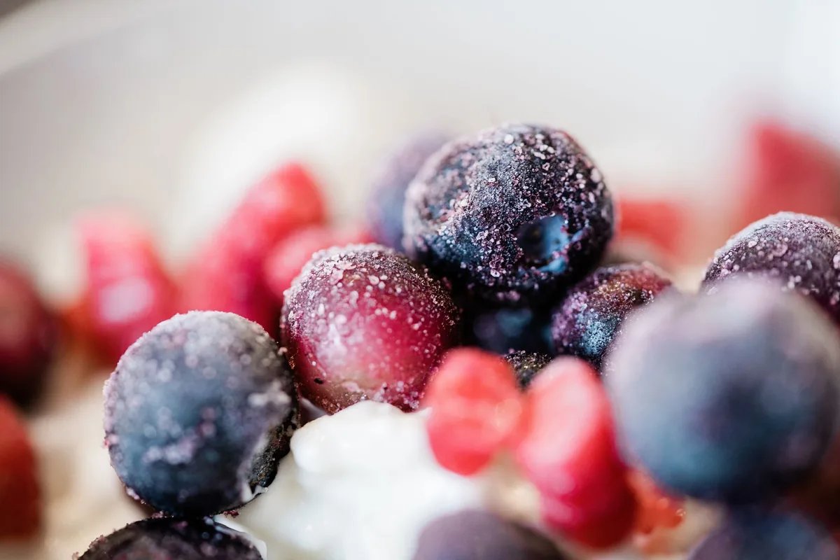 A white bowl heaped with frosted frozen raspberries and blueberries