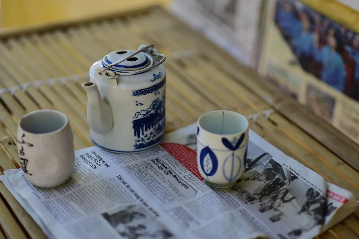 A blue and white teapot with cups on a newspaper