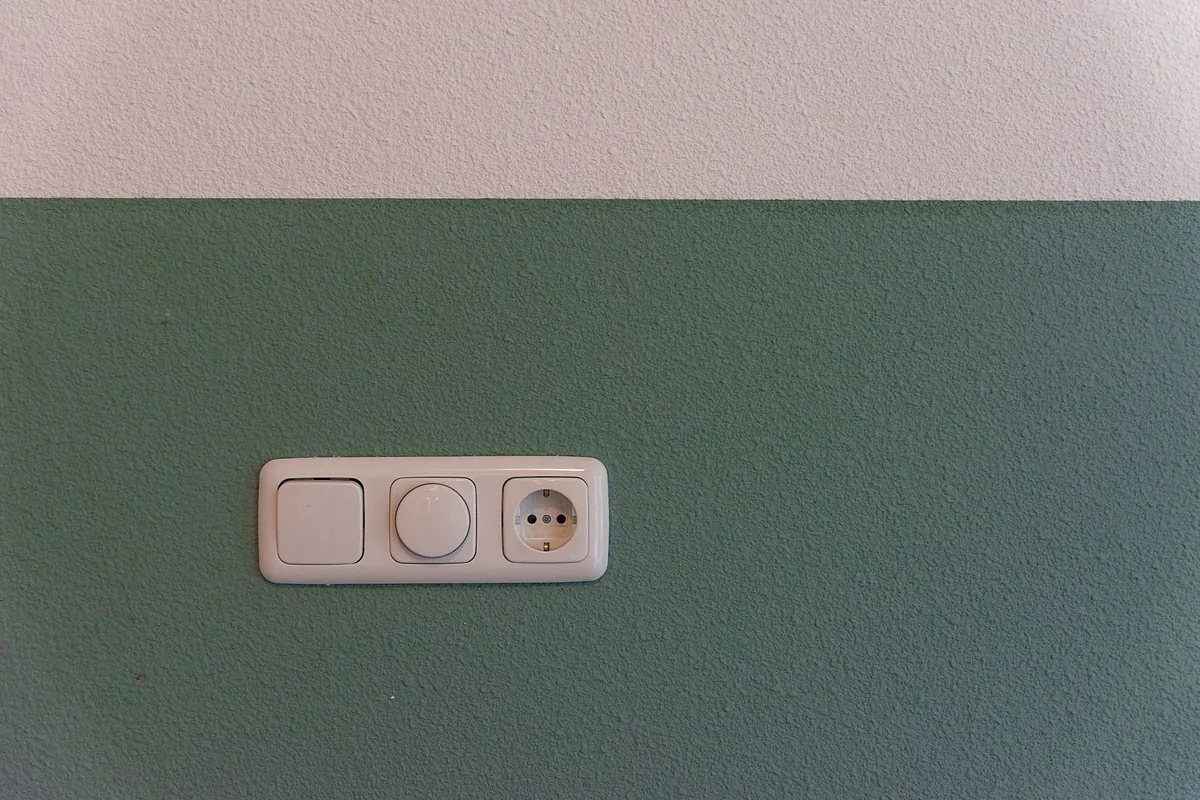 A white wall socket on a green wall