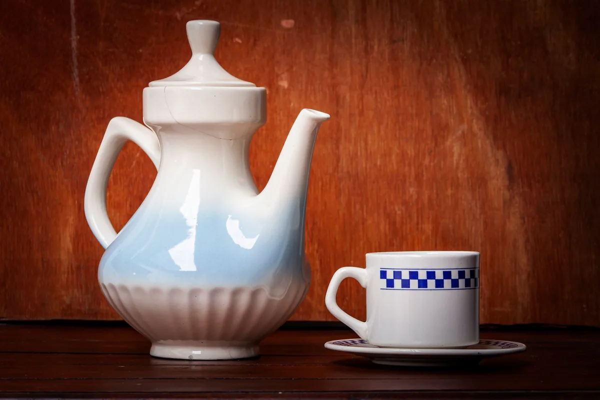 A white teapot and cup on a wooden surface