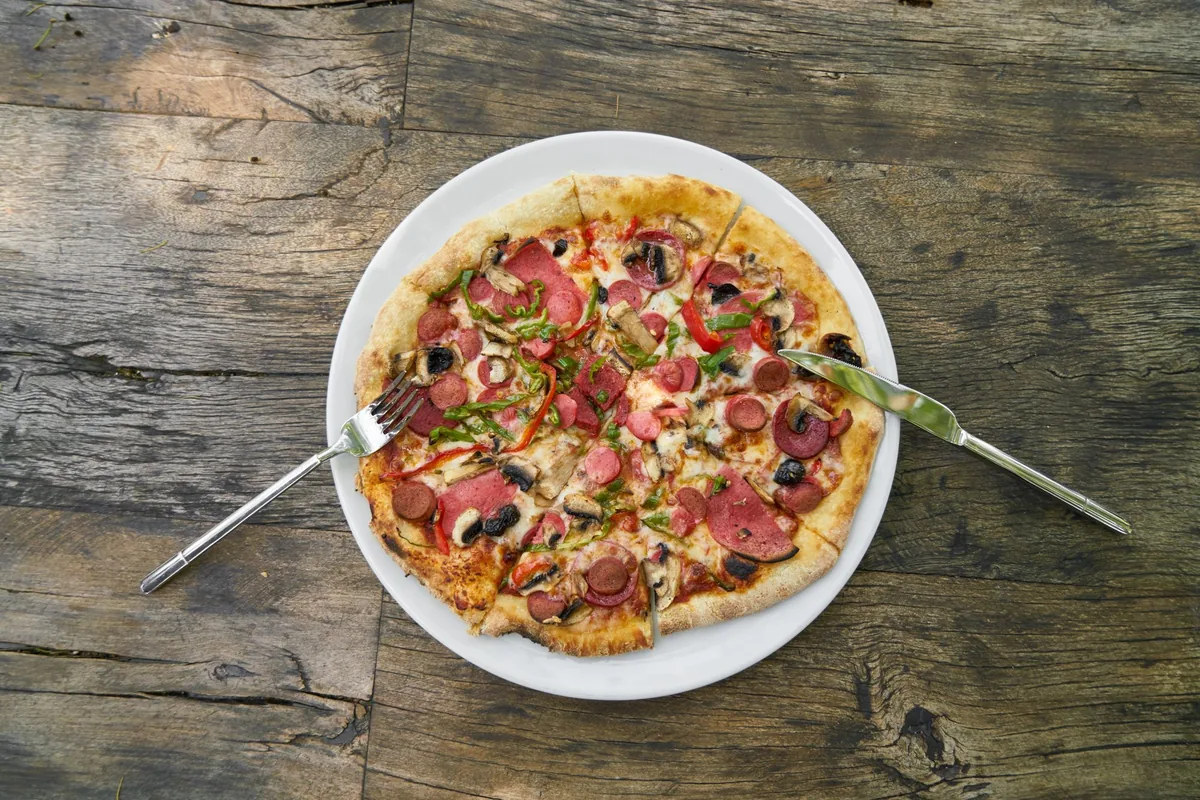 A whole pizza on a white plate on a wooden table