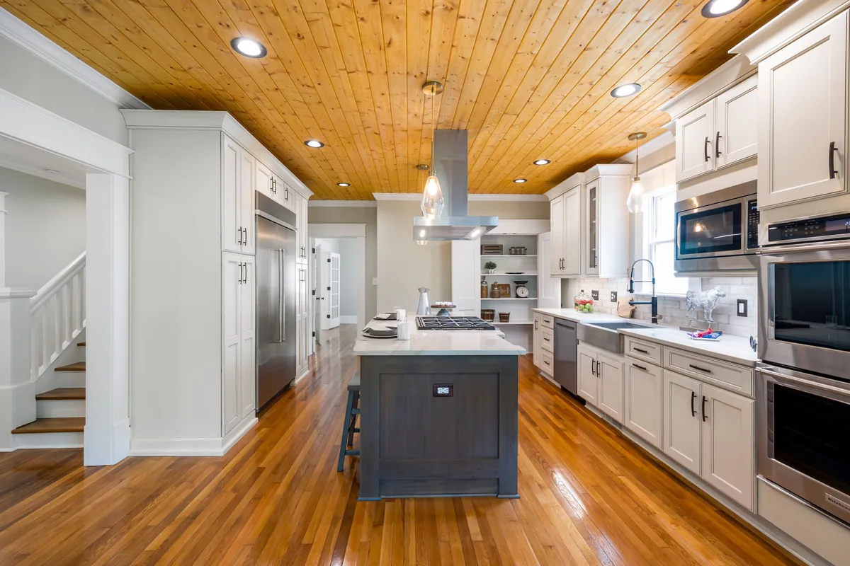 A long kitchen with a wood ceiling, an island and a chimney hood