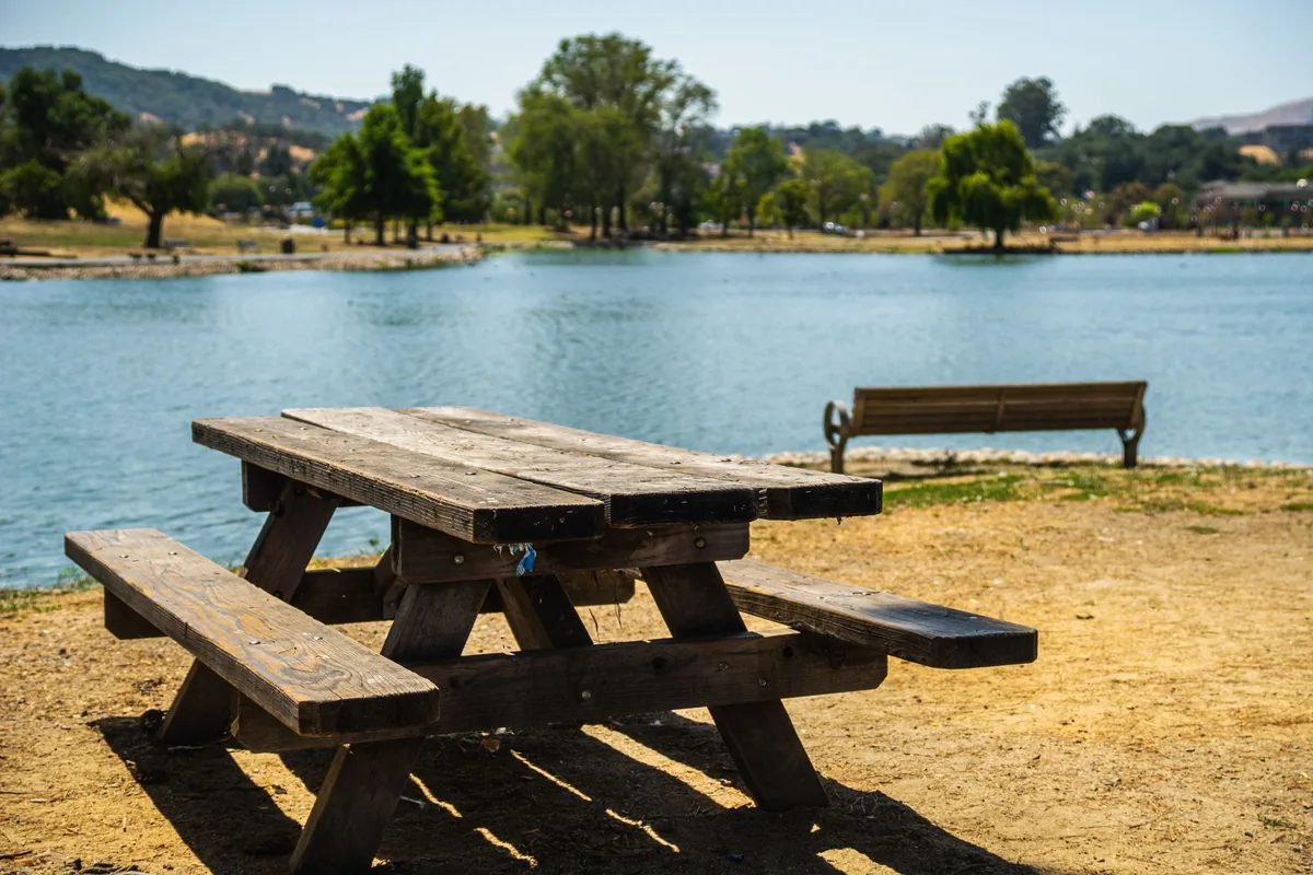 A wooden picnic table on a sandy lakeshore under a blue sky