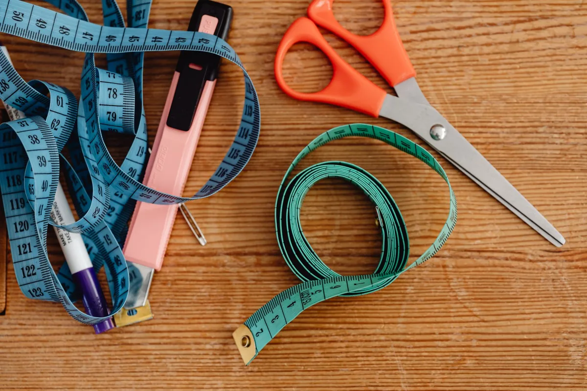 A cloth tape measure, scissors and pens on a wooden table