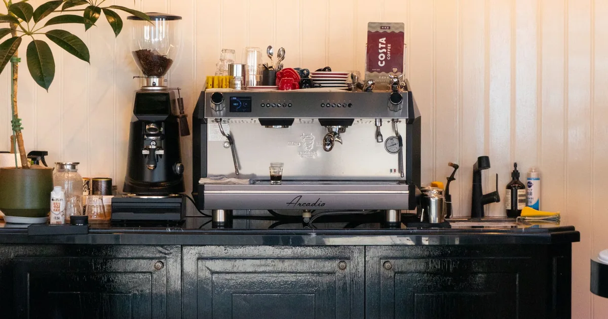 An electric coffee grinder beside a bowl of roasted coffee beans on a kitchen counter