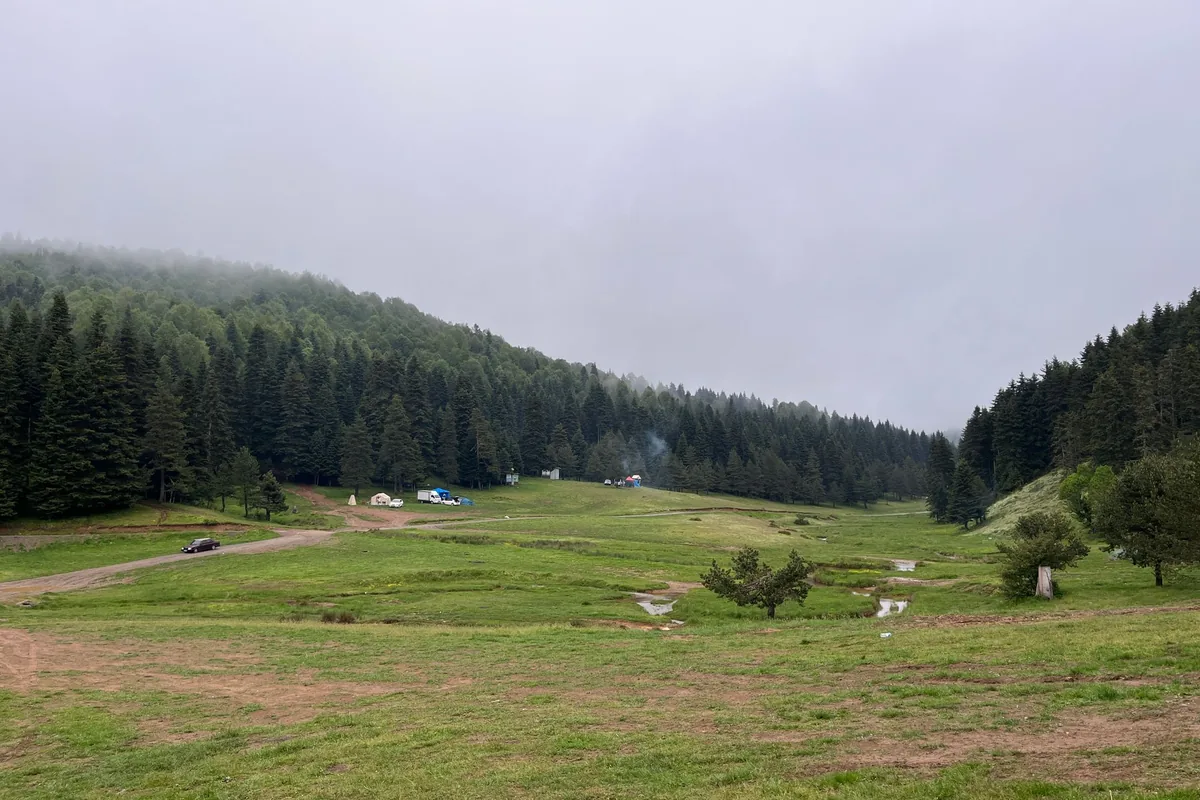 A green mountain valley campsite with tents in the distance