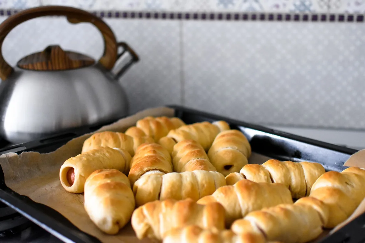 Baked rolls on a lined tray beside a kettle