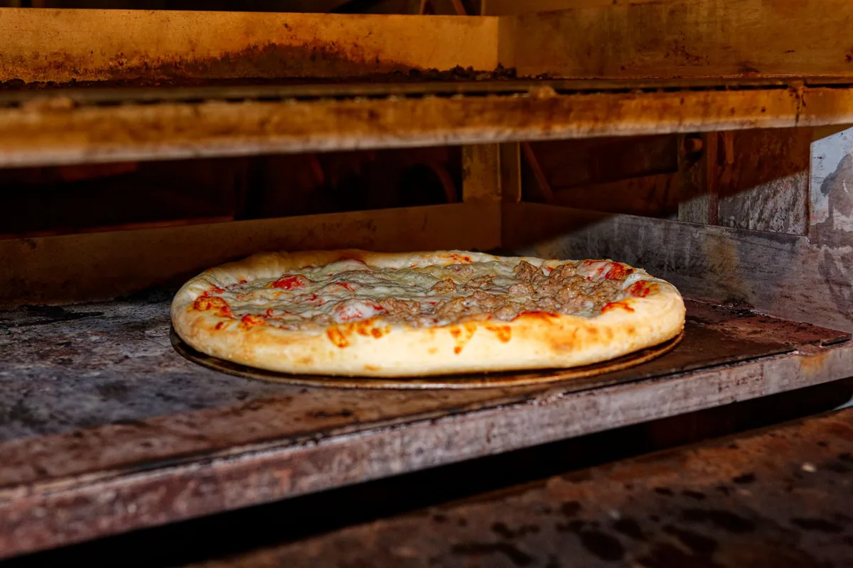A pizza baking on the floor of a stone oven