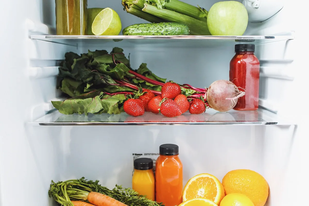 An open refrigerator with shelves of fresh vegetables, fruit and bottled water