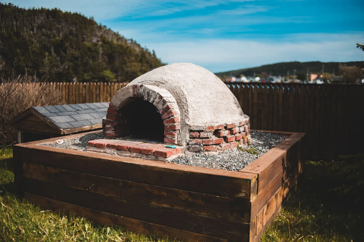 A domed clay pizza oven on a raised timber base outdoors