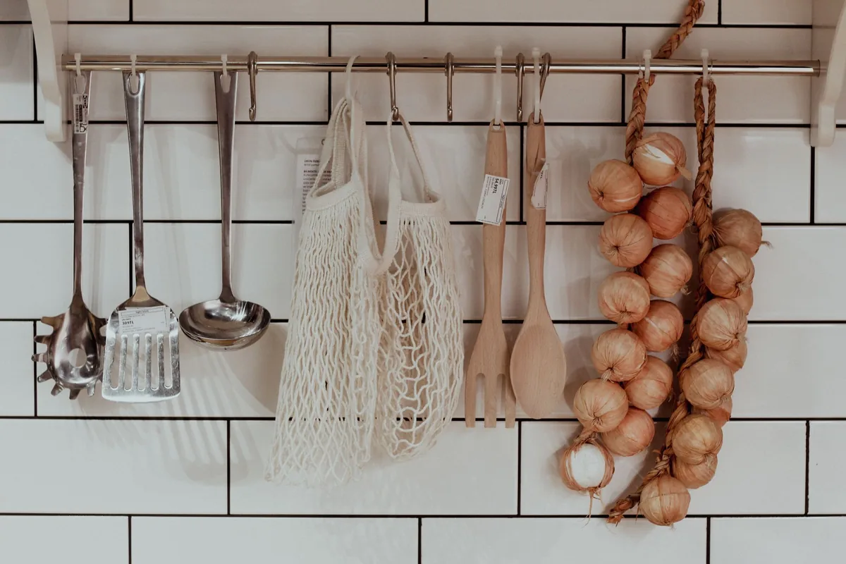 Assorted metal kitchen utensils hanging from a rail above a clean worktop
