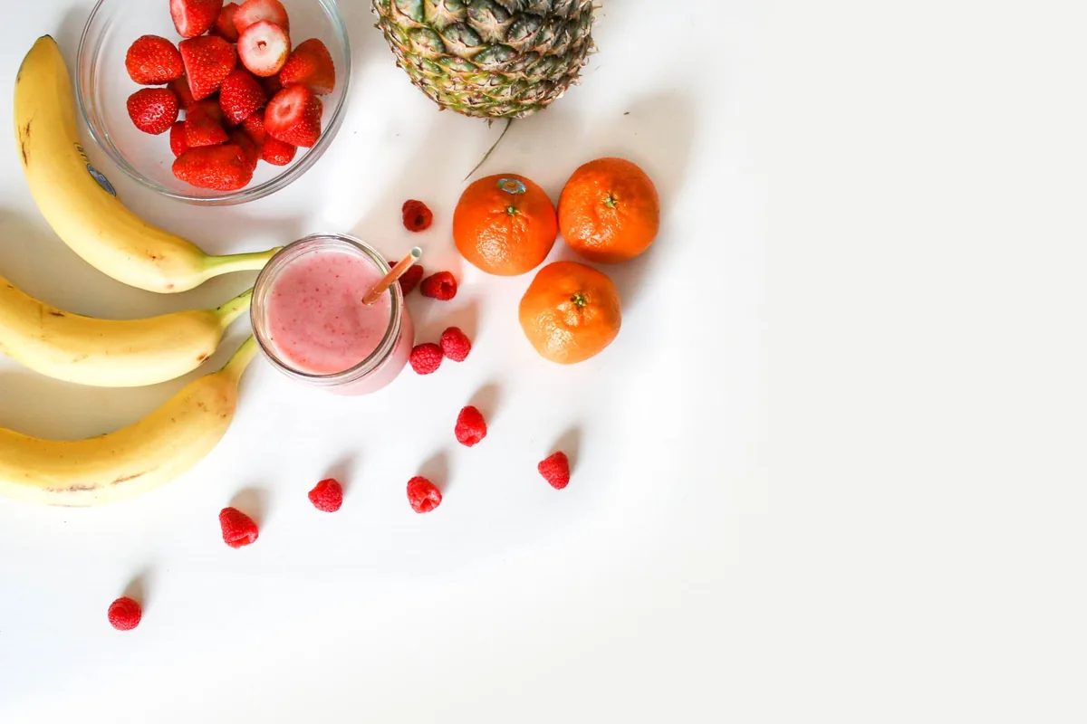 Bananas, berries and leafy greens laid out on a light kitchen counter
